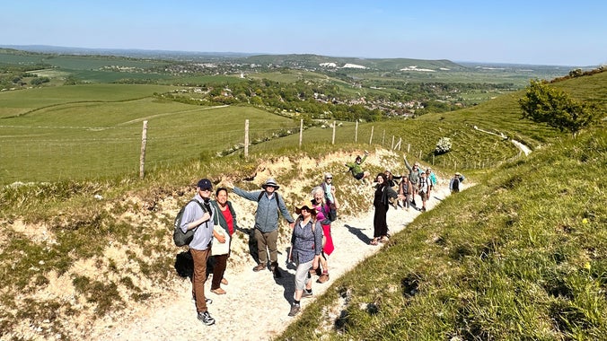 A group of people stand and wave from a sunny path on the South Downs
